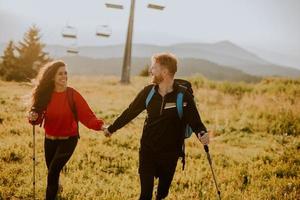 Smiling couple walking with backpacks over green hills photo