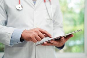 Asian man doctor using tablet computer to reading patient report, check up and search for solve treatment health medical online in hospital. photo