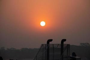 Sunset view from a ship rooftop with ship exhaust pipe silhouette. Sky horizon and sunset close-up view at dusk time. Traveling sunset photo from a launch. Beautiful twilight scenery with a red sky.