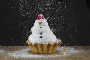 monigote de nieve magdalena Navidad pastel en un negro antecedentes rociado con Formación de hielo azúcar. hermosa invierno postre. foto