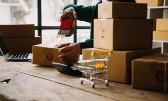 Startup small business entrepreneur or freelance Asian woman using a laptop with box, Young success Asian woman with her hand lift up, online marketing packaging box and delivery, SME concept. photo