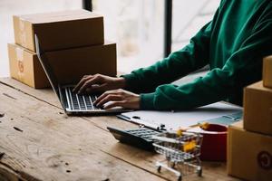 Startup small business entrepreneur or freelance Asian woman using a laptop with box, Young success Asian woman with her hand lift up, online marketing packaging box and delivery, SME concept. photo