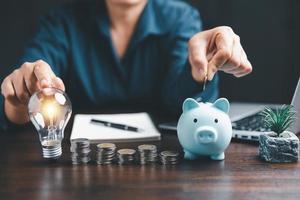 Businesswoman with lightbulb and piggy bank and using calculator to calculate and money stack. Save energy and money with accounting finance in office concept. Idea of energy saving planning in home. photo