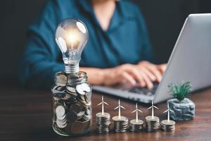 Businesswoman with lightbulb on money jar and using calculator to calculate and money stack. Save energy and money with accounting finance in office concept. Idea of energy saving planning in home. photo