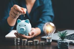 Businesswoman with lightbulb and piggy bank and using calculator to calculate and money stack. Save energy and money with accounting finance in office concept. Idea of energy saving planning in home. photo