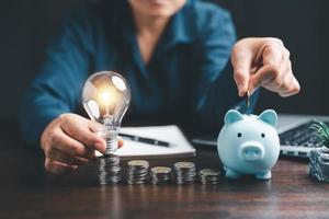 Businesswoman with lightbulb and piggy bank and using calculator to calculate and money stack. Save energy and money with accounting finance in office concept. Idea of energy saving planning in home. photo