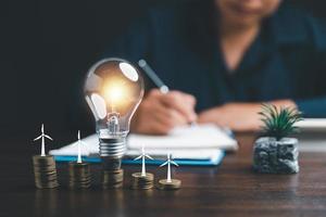 mujer de negocios con bombilla en monedas y utilizando calculadora a calcular y dinero pila. salvar energía y dinero con contabilidad Finanzas en oficina concepto. idea de energía ahorro planificación en hogar. foto