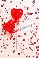 Valentine's Day. Date of February 14 and two curly red hearts on a pink background strewn with hearts. Vertical and top view photo