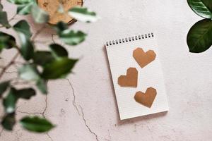 Eco mock up. Craft hearts on an open notepad on a light concrete background and plant home leaves. Top view. photo