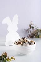 A bowl of quail eggs and a white rabbit on the table for a happy easter. Vertical view photo