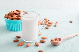 Fresh almond milk in a glass and almonds in a wooden spoon on a light background. Alternative nutrition, source of vitamins photo