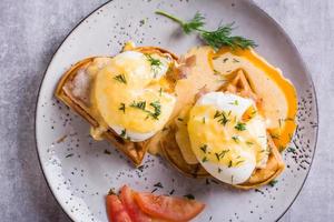 Closeup of eggs benedict and bacon on a crispy waffle for homemade breakfast. Top view photo