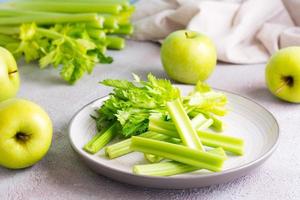 Sliced fresh celery stalk with leaves on a plate and green apples on the table ready to be cooked. Vegetarian food photo