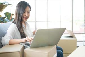 Happy young Asian woman entrepreneur, Smile for sales success after checking order from online shopping store in laptop at home office, Concept of merchant business online and eCommerce photo