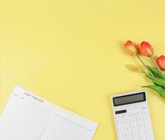 flat layout of Habit tracker book,  white calculator and tulips on yellow background. photo