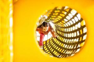 Little girl move on in pipe at yellow playground park in active entertaiments. photo