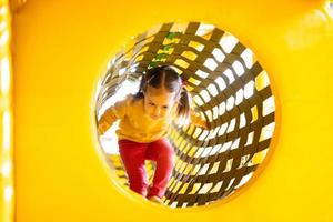 Little girl move on in pipe at yellow playground park in active entertaiments. photo