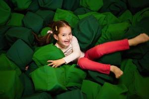 Little girl kid lies on green soft cubes at playground park. Child in active entertaiments. photo