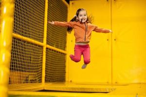 pequeño niña niño saltando en trampolín a amarillo patio de recreo parque. niño en movimiento durante activo entretenimientos foto