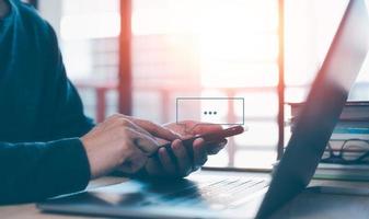 social media text messaging concept, man using smartphone texting message while sitting on table with computer laptop in office with warm morning or evening photo