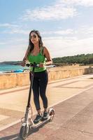 mujer montando eléctrico scooter, contento y verano paseo a tropical isla playa recurso para vacaciones. ciudad, calle y eco simpático transporte, divertido en escolta en fiesta en mallorca,baleares isla foto