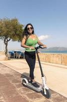 mujer montando eléctrico scooter, contento y verano paseo a tropical isla playa recurso para vacaciones. ciudad, calle y eco simpático transporte, divertido en escolta en fiesta en mallorca,baleares isla foto