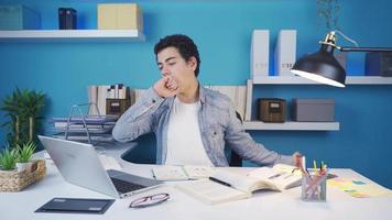 le Jeune homme obtient ennuyé de en train d'étudier une lot et départs à tomber endormi à le sien bureau. fatigué de travail en retard, le Jeune homme lentement commence à tomber endormi à le tableau. video