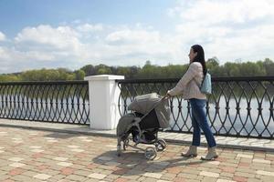 joven chica, madre con un paseante caminando en el parque por el río. de la madre día. foto