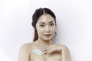 piel cuidado productos concepto. asiático mujer aplicando hidratante loción en cuerpo después ducha, en pie envuelto en toalla, recortado imagen foto