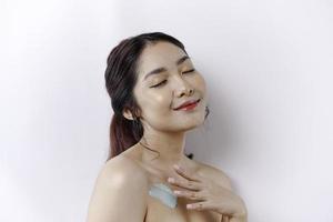 piel cuidado productos concepto. asiático mujer aplicando hidratante loción en cuerpo después ducha, en pie envuelto en toalla, recortado imagen foto