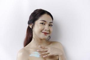 Skin Care Products Concept. Asian woman applying moisturizing lotion on body after shower, standing wrapped in towel, cropped image photo