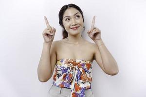 Excited Asian woman pointing at the copy space on top of her, isolated by white background photo