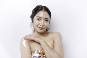 Skin Care Products Concept. Asian woman applying moisturizing lotion on body after shower, standing wrapped in towel, cropped image photo