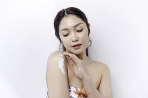 Skin Care Products Concept. Asian woman applying moisturizing lotion on body after shower, standing wrapped in towel, cropped image photo