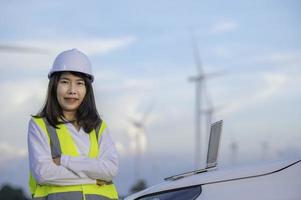 women engineer working and holding the report at wind turbine farm Power Generator Station on mountain,Thailand people photo