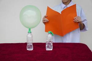 Closeup student study science experiment about reaction of chemical in bottles and balloons. Read  the result of experiment in book. Concept, science subject activity, education. Learning by doing photo