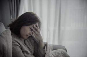 mujer asiática enferma sentada en el sofá, quédese en casa, la mujer se sintió mal, quería acostarse y descansar, fiebre alta foto