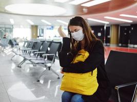 mujer con cerrado ojos médico máscara esperando pasajero con equipaje foto