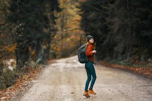 happy traveler with backpack walks on the road in autumn forest photo