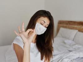 woman gesturing with hand in medical mask in bedroom photo