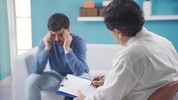 psicólogo maduro hombre tratando su joven adulto masculino paciente. médico sentado en silla hablando a Deprimido paciente en psicoterapia sesión. video