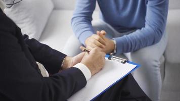 Male psychologist taking notes in his diary and listening to his male patient during psychotherapy session. video