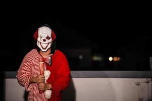 asiático hermoso hombre vestir payaso máscara con arma a el noche escena, halloween festival concepto, terror de miedo foto de un asesino en naranja tela, mal payaso charactor