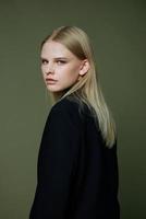 A close portrait of a blonde looking over her shoulder in a black jacket posing in a studio on a green background. The concept of stylish fashion photography photo