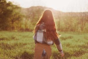 un mujer carreras a través de un campo con su espalda a el cámara en un verano día con su pelo largo y volador en el puesta de sol. el concepto de libertad y armonía con naturaleza foto