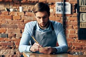 a man in an apron sits at a table accepting an order a cafe waiter photo