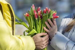 un joven Pareja en amor en el calle, participación flores en su manos a un romántico momento. un hombre da rojo tulipanes a un rubia mujer.la concepto de el primavera fiesta es marzo 8, Pascua de Resurrección, De las mujeres día foto