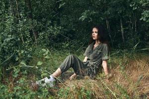 Surprised woman in jumpsuit sneakers sits on the grass in the forest photo