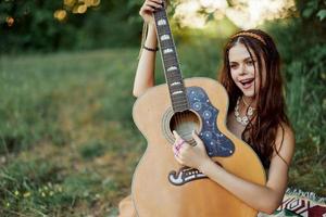 Beautiful woman playing guitar in nature in a hippie summer look, singing songs style of life without worries photo