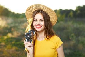 Smiling woman with camera in hands wearing hat red lips yellow t-shirt nature photo